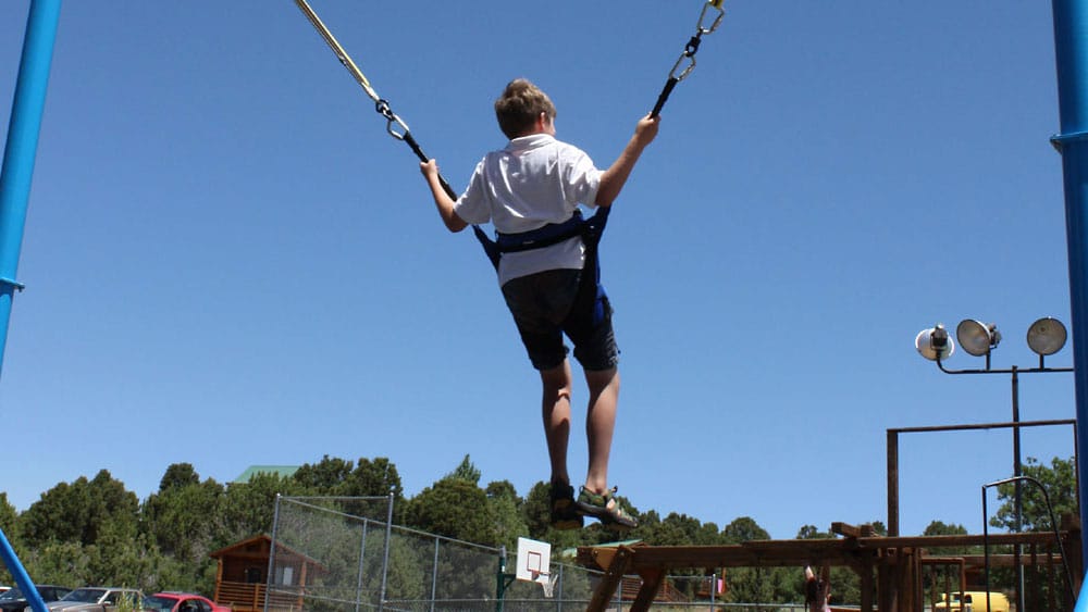 A child swings high on a playground swing set against a clear blue sky.
